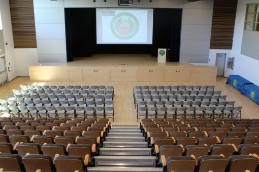 View from the top of the bleachers in the Kenora campus event centre facing a large stage and pull-down screen