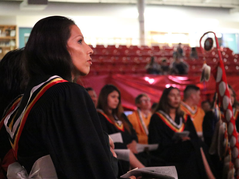 Female graduate looking up, sitting among her fellow graduates at a graduation ceremony