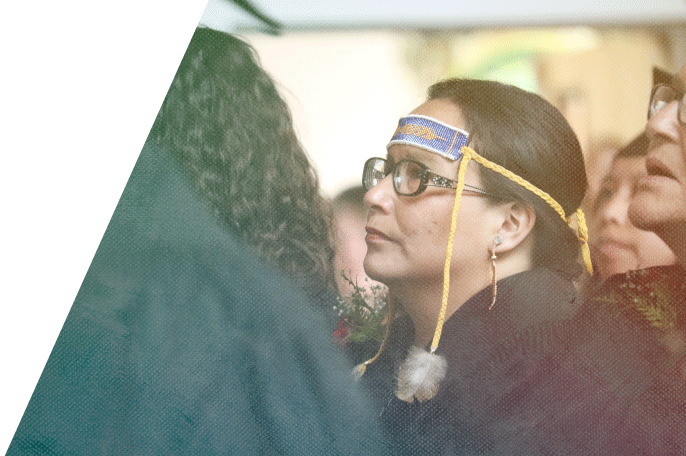 Anishinaabe woman sitting amongst fellow graduates at a graduation ceremony