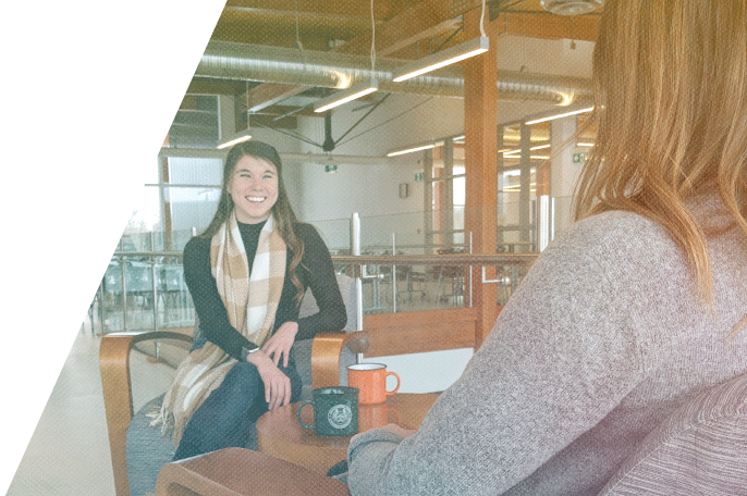 Two women facing each other sitting at a small table with coffee cups