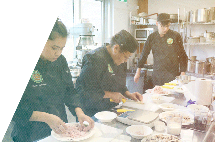 Culinary students dredging chicken in flour in SGEI's culinary lab