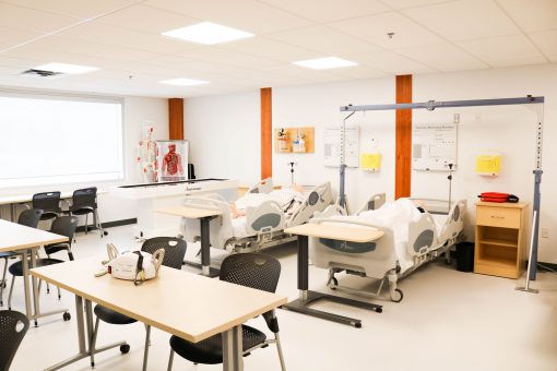 View of SGEI health disciplines lab equipped with hospital beds, a bed lift, and a skeletal model