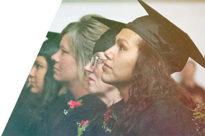 Anishinaabe woman sitting amongst fellow graduates at a graduation ceremony