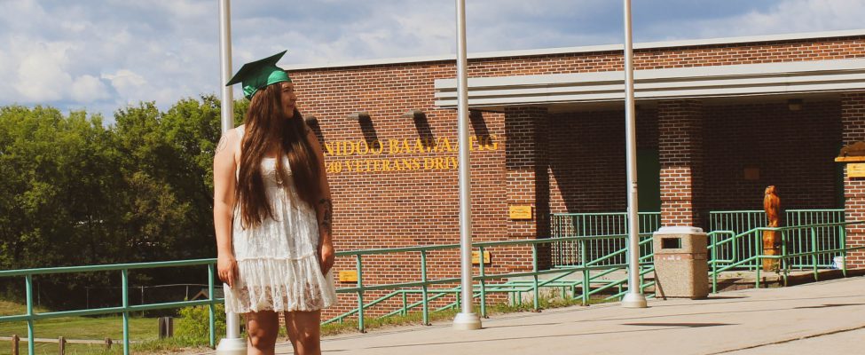 A graduate standing proudly outside of the school building