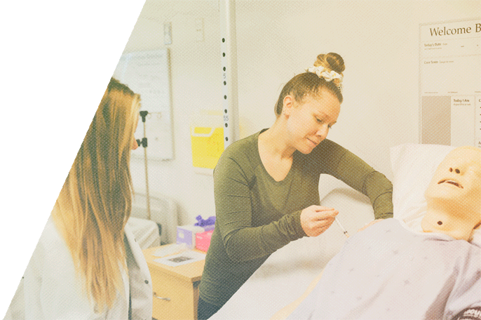 SGEI student inspecting a mannequin laying in a hospital bed in SGEI's health disciplines lab