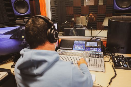 Man sitting at a desk adjusting audio controls in front of a soundproof room