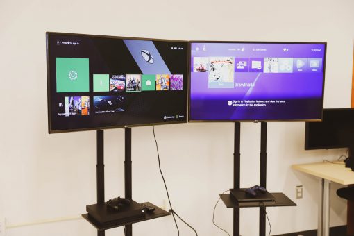 Set of two large monitors displaying Xbox and PlayStation menus