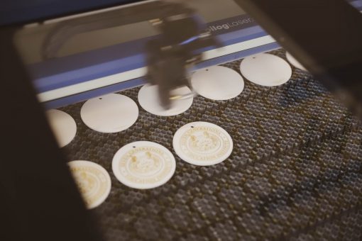 Inside of a laser engraver with wooden disks being engraved with the SGEI logo