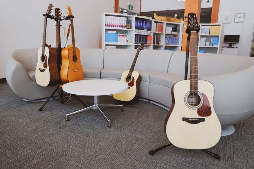 Collection of five acoustic guitars on stands and leaning against a curved grey couch in a library