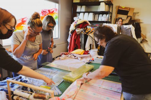 Group of four women around a table measuring and cutting fabric for ribbon skirts