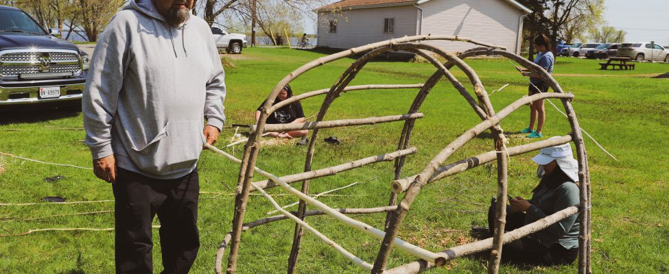 Man standing beside traditional smoke hut structure