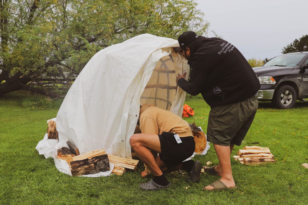 Two men securing a tarp around a traditional smoke hut