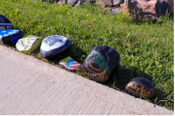 A group of painted rocks lined up against a sidewalk