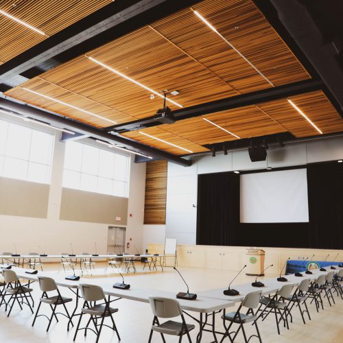 Large auditorium with tables and chairs formed in a u-shape, a stage, and large projector screen