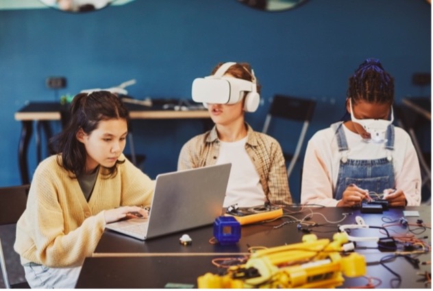 A group of women use virtual reality (VR) headsets to interact and build during engineering class