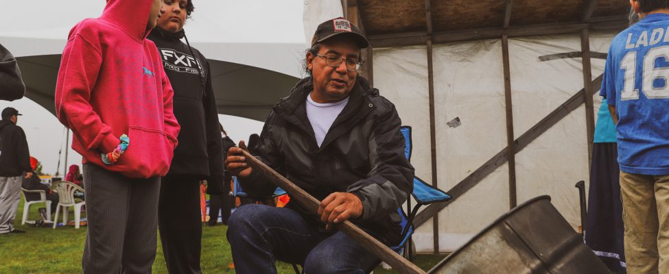 Anishinaabe man parching wild rice as a group of youth observe and learn