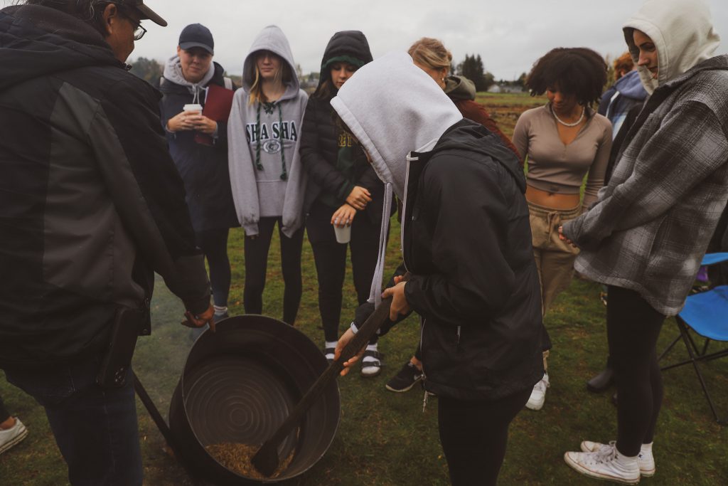 A group of youth learn about wild rice parching from a local elder