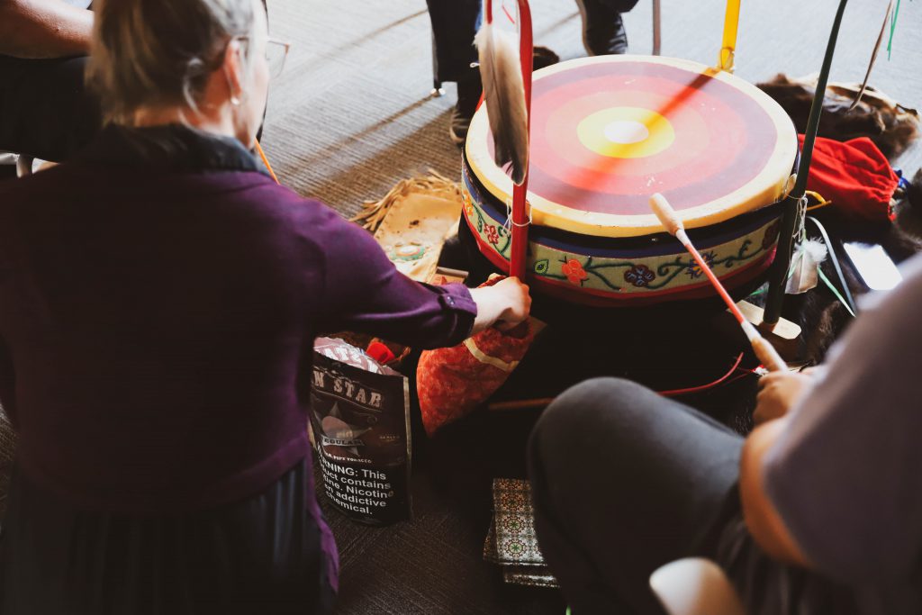 Woman offering tobacco beside a traditional Anishinaabe drum.
