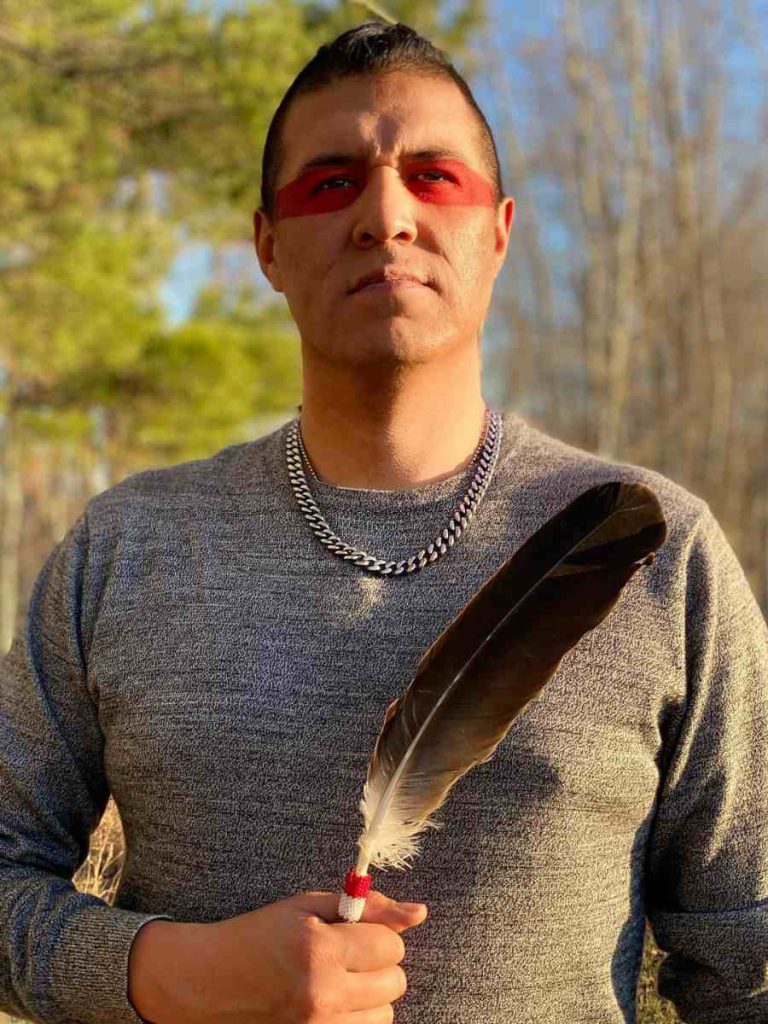 Anishinaabe man wearing war paint and holding a feather