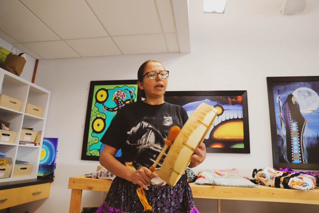 Anishinaabekwe playing a hand drum and singing