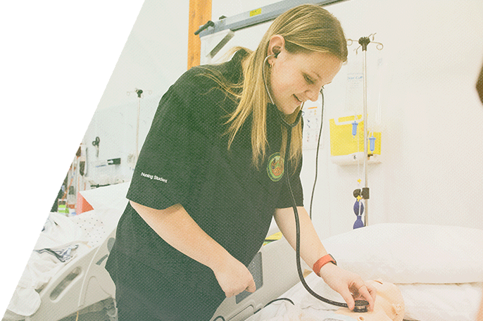 A nursing student uses a stethoscope on a mock infant patient.