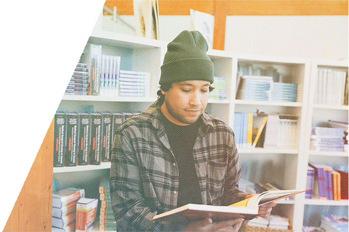 Anishinaabe student with a beanie on reading a book in a library.