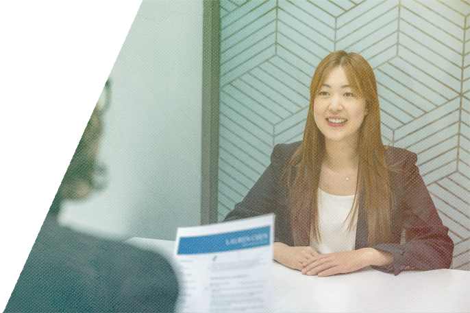 Smiling woman sits at a table in front of a person looking at her resume.