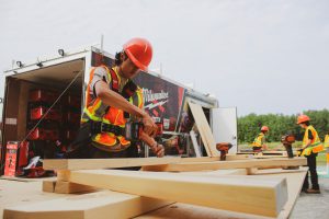 Man in orange PPE drilling into a piece of wood