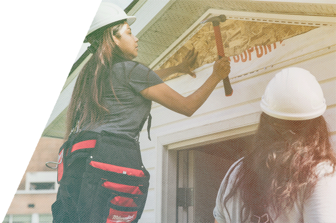 Woman wearing construction helmet hammering a shed
