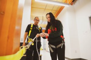 IMG_2090 1 Young woman standing next to an older man holding a harness for working at heights training