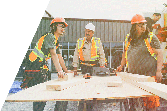 Three male construction workers standing over a sheet of plywood